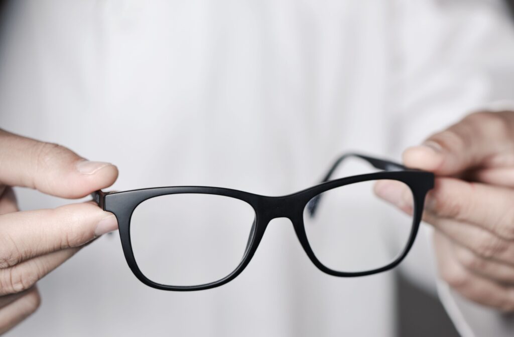 Close-up of two hands holding simple black framed glasses.